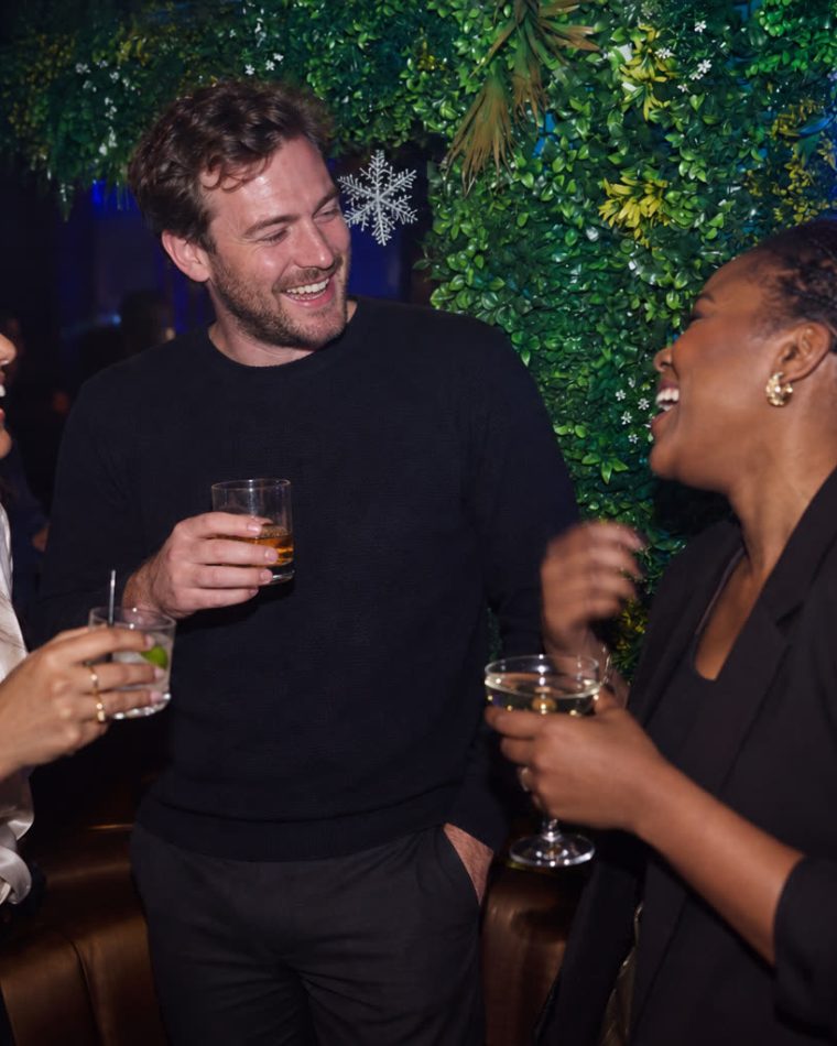 Three people with drinks beside the foliage wall at Cabo.